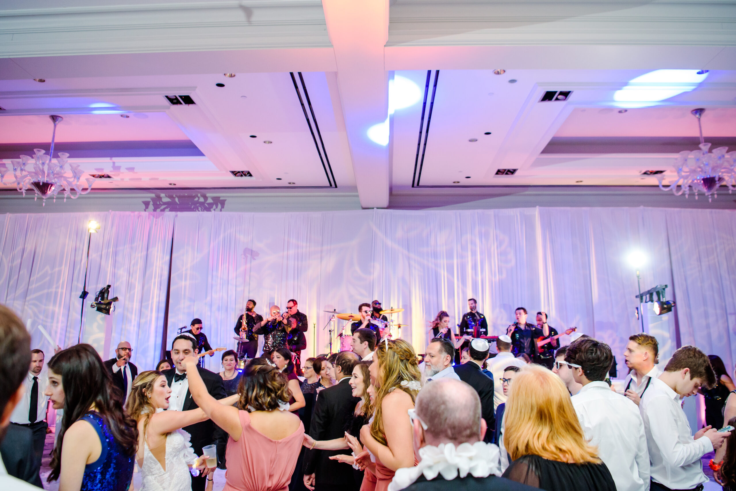 Lively wedding reception with guests dancing and band performing on stage.